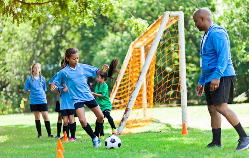 A young girl at soccer practice while her coach looks on