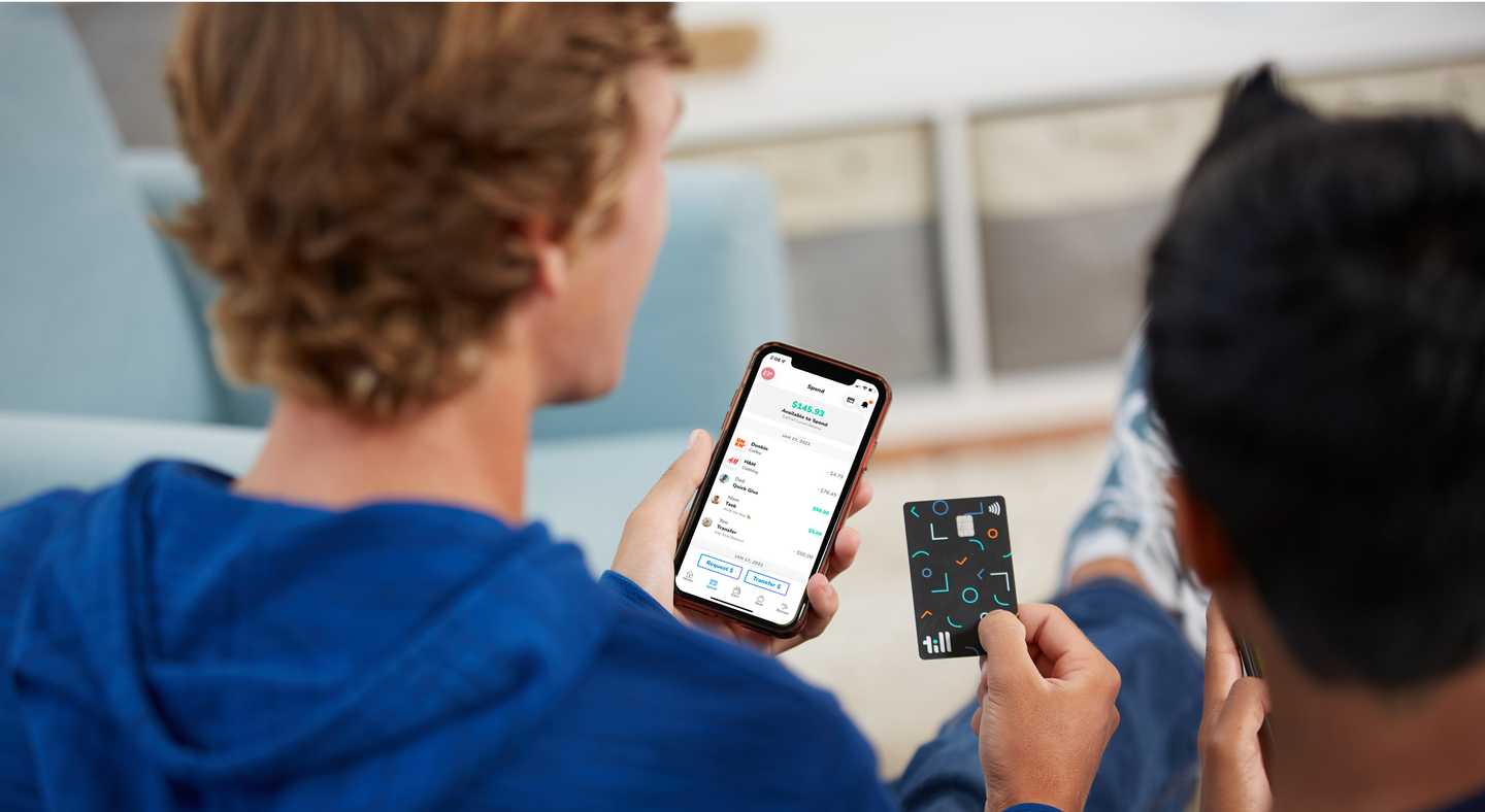 Teenager holding a Till debit card and a phone with the Till Financial app opened on the spending page