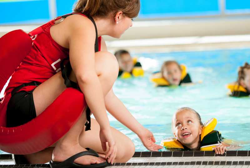 A young female lifegaurd assisting a new child swimmer