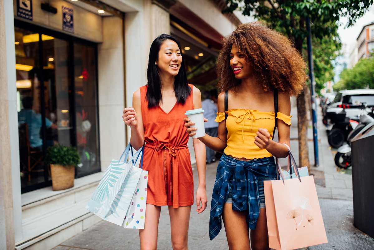 Two teenagers walking in the street with shopping bags and coffee in their hands