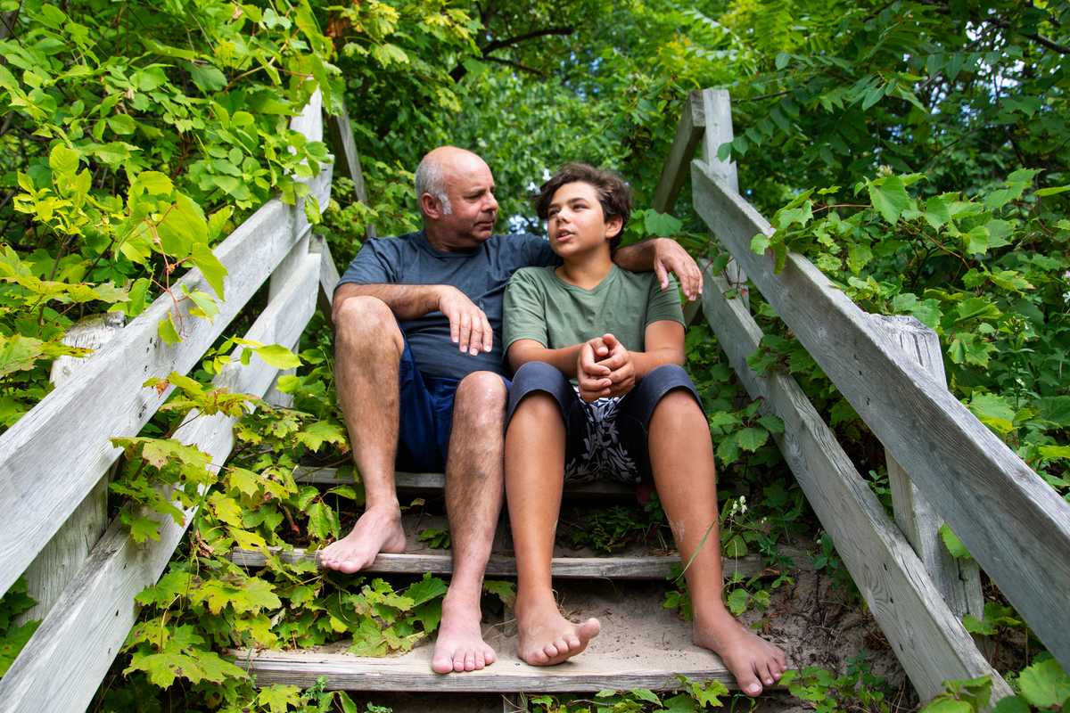 A father sitting beside his son, talking to him with his arm around his shoulder