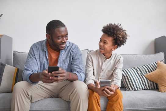 Father and Son talking while using thier phones on the couch